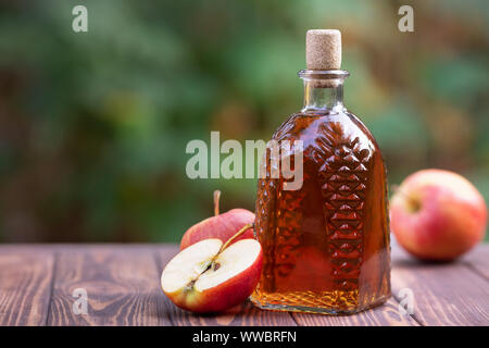 Apple Cider oder Essig in Glas Dekanter und Reife frische Äpfel auf hölzernen Tisch im Freien Stockfoto