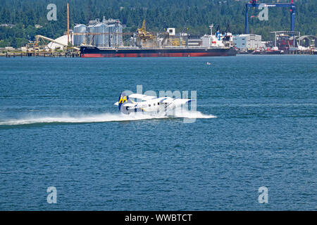 Ein Harbour Air Wasserflugzeug in den Hafen von Vancouver mit Seaspan im Hintergrund, Vancouver, B.C., Kanada. Juni 15, 2019 Stockfoto