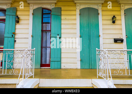 New Orleans, USA - 22. April 2018: Grün, Blau und Weiß mit gelben Tür Eingang oder direkt vor der Tür Home Haus Architektur mit französischen Fenstern Rollläden Stockfoto
