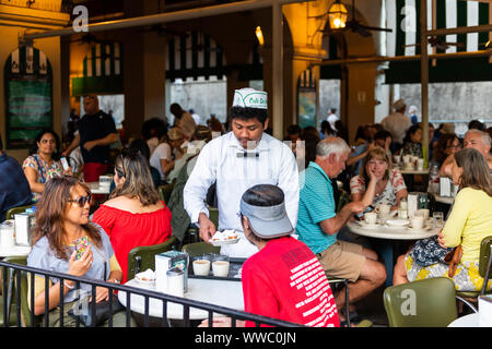 New Orleans, USA - 22. April 2018: die Menschen in dem berühmten Café Du Monde Restaurant essen beignet Puderzucker Donuts, Kaffee trinken Chicoree durch w serviert. Stockfoto
