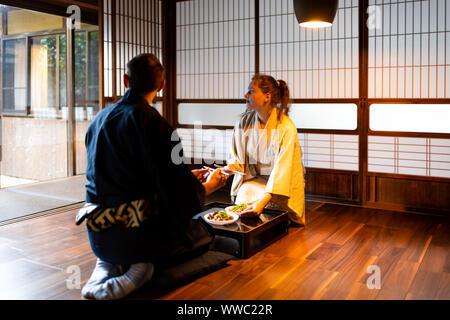 Paar Mann und Frau im Kimono Seiza sitzen, Essstäbchen und Essen an traditionellen Japanischen Home Zimmer durch Tabelle Platten von Shoji Schiebetüren pa Stockfoto