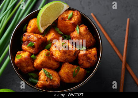 Paneer Mandschurischen oder Paneer 65 in der Schüssel am Schwarzen konkreten Hintergrund. Paneer mandschurischen ist indische, chinesische Küche Teller mit panner Käse, Tomaten, auf Stockfoto