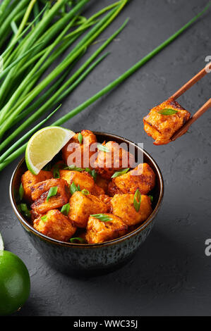 Paneer Mandschurischen oder Paneer 65 in der Schüssel am Schwarzen konkreten Hintergrund. Paneer mandschurischen ist indische, chinesische Küche Teller mit panner Käse, Tomaten, auf Stockfoto