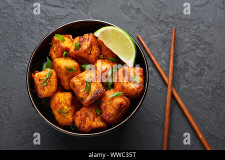 Paneer Mandschurischen oder Paneer 65 in der Schüssel am Schwarzen konkreten Hintergrund. Paneer mandschurischen ist indische, chinesische Küche Teller mit panner Käse, Tomaten, auf Stockfoto