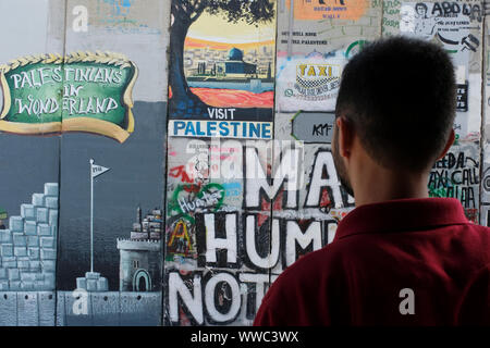 Ein palästinensischer Mann sieht die Trennung Barriere oder eine Wand mit Graffiti Slogans von Touristen am Rande der Stadt Bethlehem im Central West Bank gesprüht. Palästinensische Gebiete, Israel Stockfoto