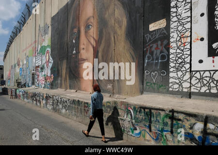 Eine Palästinenserin kommt an einem gemalten Bild vorbei, das Ahed Tamimi, einen 17-jährigen palästinensischen Aktivisten gegen die israelische Besatzung zeigt, gemalt auf der Trennungsmauer oder Mauer, die von Israel am Stadtrand von Bethlehem im zentralen Westjordanland errichtet wurde. Palästinensische Gebiete Stockfoto