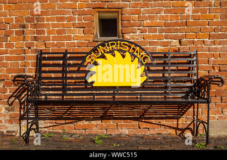 Sonnenaufgang-Schild in Metallbank vor roter Ziegelwand Stockfoto