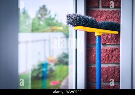 Gelb, Blau und Schwarz Poly Push Besen lehnte sich gegen das Glas und die Red Brick Wall im Schlamm. Halten Sie Ihre Umwelt sauber und ordentlich Konzept. Stockfoto