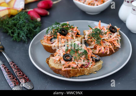 Hausgemachte Sandwiches mit Möhren und Radieschen, mit gekochtem Ei und schwarzen Oliven in einer Platte gegen einen dunklen Hintergrund eingerichtet Stockfoto