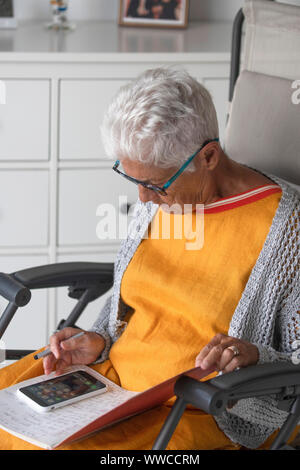 Eine ältere Person verwendet ein Mobiltelefon durch Lesen von Notizen Stockfoto