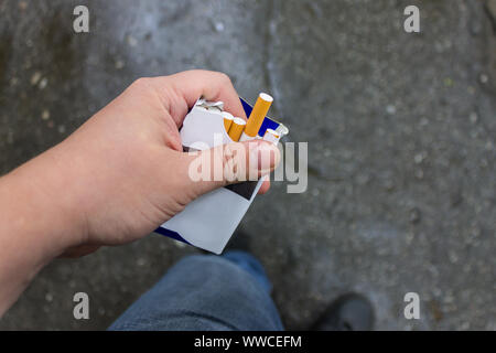 Eine Packung Zigaretten in den Händen eines Rauchers und eine längliche Zigarette Stockfoto