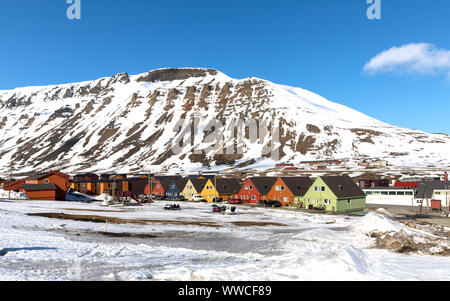 Reihe von bunten chalet Häuser in Longyearbyen auf Spitzbergen. Blauer Himmel und die Berge im Hintergrund mit Schneemobilen im Vordergrund geparkt. Stockfoto