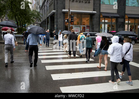 Fußgänger mit Sonnenschirmen überqueren Zebrastreifen an der North Michigan Avenue Magnificent Mile auf einem nassen bewölkten Tag in Chicago Illinois USA Stockfoto