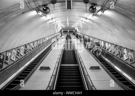 Monochrome Ansicht mit Blick auf die Rolltreppen in der U-Bahn-Station London. Schwarz-weiße Vorderansicht der Passagiere, die die Rolltreppe hinunter fahren. Stockfoto