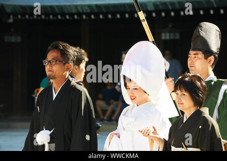 Eine Braut in Weiß und Bräutigam in schwarzem formalen Kimono Spaziergang unter einem großen Regenschirm während der traditionellen Shinto Hochzeitszeremonie am Meiji Jingu Schrein. Stockfoto