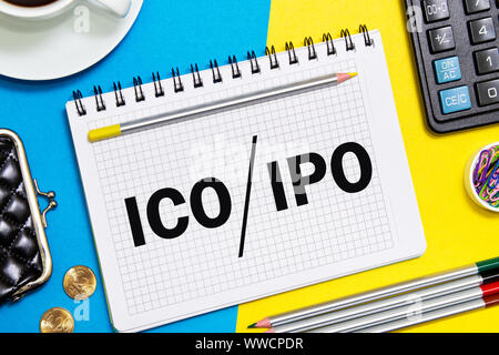 Ein Notebook mit Geschäft Anmerkungen erste Münze mit ICO vs IPO Initial Public Offering mit Office Tools auf Gelb blauen Hintergrund. Konzept der ch Stockfoto