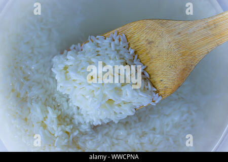 Flache Oberseite legen Blick hinunter von eingeweichten Reis, Getreide, trübe Flüssigkeit Wasser in Glasschale, Huhn und wilder Reis Suppe. kochen Hausgemachte frische cremige Suppe Hoch Stockfoto