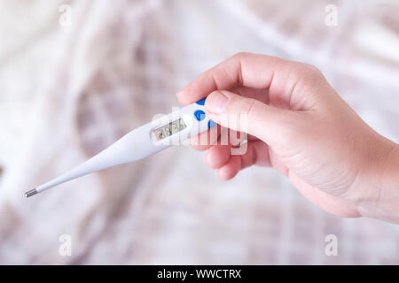 Closeup Schoß einer Frau an Thermometer suchen. Weibliche Hände halten ein digitales Thermometer. Mädchen misst die Temperatur. Flache Tiefenschärfe mit Stockfoto