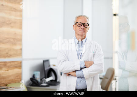 Taille bis Portrait von leitenden Arzt Brille mit Kamera beim Stehen mit der Waffe in der modernen Klinik gekreuzt, kopieren Raum Stockfoto