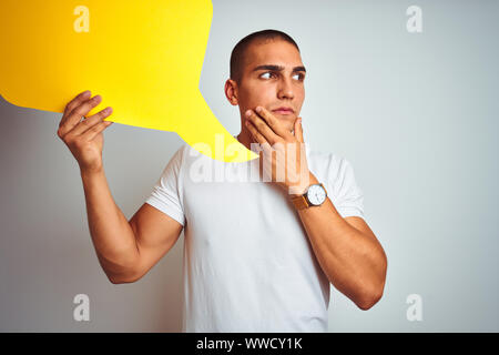 Junger Mann mit gelben Sprechblase über Weiß isoliert Hintergrund ernstes Gesicht denken über Frage, sehr verworrene Vorstellung Stockfoto