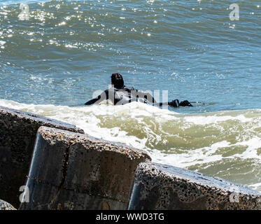 Ein Surfer ist die Überschrift, die in den Ozean neben einem steinernen Steg von Fire Island National Sea Shore Long Island New York. Stockfoto