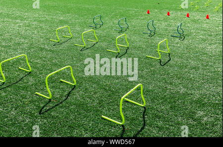 Gelbe Mini Hürden und orange Kegel werden auf einem Rasenfeld für Geschwindigkeit und Agilität der Praxis gesetzt. Stockfoto