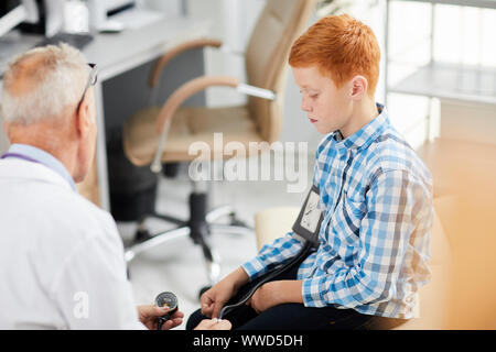 Portrait von leitenden Arzt Blutdruck messen von niedlichen rothaarigen Jungen während der Konsultation in Kind Healthcare Clinic, kopieren Raum Stockfoto