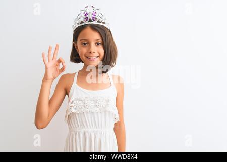 Schönes kind Mädchen mit Princess Crown stehend über isoliert weißer Hintergrund Lächeln positive tun ok Zeichen mit der Hand und der Finger. Erfolgreiche e Stockfoto