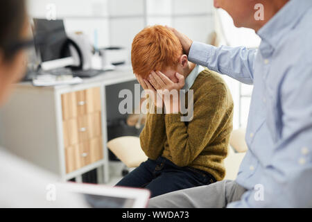 Portrait von traurigen rothaarigen Jungen weinend in ärzte Büro während Termin, verstecken Gesicht in mit Vater tröstete ihn, kopieren Raum Stockfoto