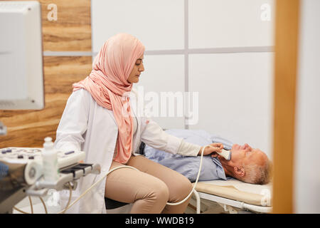 Seitenansicht Portrait der junge arabische Ärztin Durchführen von Ultraschall bis auf ältere Patienten in der medizinischen Klinik prüfen, kopieren Raum Stockfoto