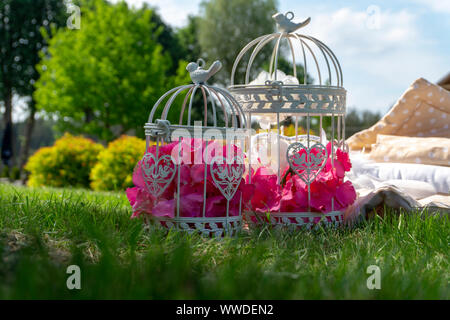 Zwei weiße Käfige mit rosa Blumen im Freien auf frische grüne Gras gefüllt neben einem Stapel von Bettwäsche oder Bettwäsche in einem Spring Park Stockfoto