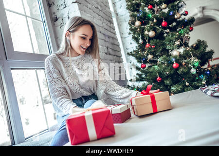 Weihnachten, Weihnachtsmusik, x-mas, Winter, Glück Konzept - lächelnde Frau mit vielen Geschenkboxen. Mädchen öffnet ein Geschenk vor dem Hintergrund der Weihnachtsbaum. Happ Stockfoto