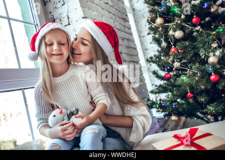 Glückliche Familie, Mutter und Kind Mädchen in Santa hat in der Nähe einen Weihnachtsbaum mit Weihnachtsgeschenk Stockfoto