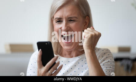 Nahaufnahme der älteren Frau schrie aufgeregt, Verwenden von Telefon, Erfolg feiern. Stockfoto