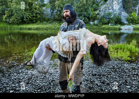 Der Fischer fand eine hilflose Frau in einem Abendkleid am Flussufer und trägt sie in die Arme. Ein Tieftraurig Dorfbewohner rettet eine Dame, die im Ohnmächtigen Stockfoto