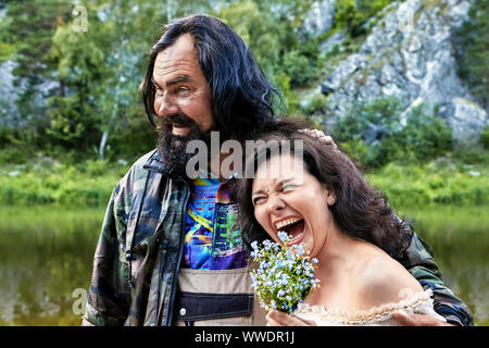 Ungekämmt, Shaggy ältere Mann umarmt von lachenden Frau mittleren Alters. Freundliche Paar aus ländlichen Gebieten posiert für ein Foto in der Natur, rauh und Stockfoto
