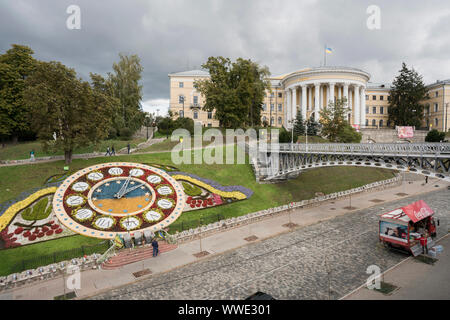 Blumenuhr und Euromaidan Denkmäler an Heroyiv Nebesnoyi Sotni Alley mit den Performing Art Center, der Oktober Palast des Gewerkschaftsbundes der Ukraine, auch als internationales Zentrum für Kultur und Kunst in der Instytutska Street in der Nähe von Independence Square im Hintergrund bekannt. Pecherskyi Bezirk, Stadtzentrum, Kiew, Ukraine, Europa Stockfoto