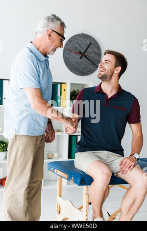 Fröhliche bärtigen Mann in Gläsern Händeschütteln mit glücklichen Patienten in der Klinik Stockfoto