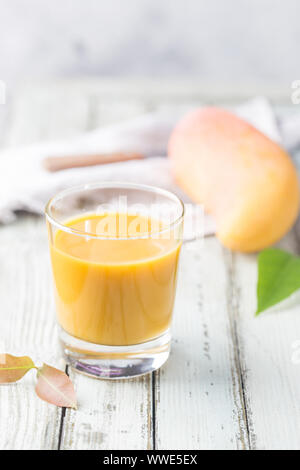 Tropische Mango Smoothie in ein Glas und frischer Mango auf einem hellen Hintergrund. Mango schütteln. Tropische Früchte Konzept. Stockfoto