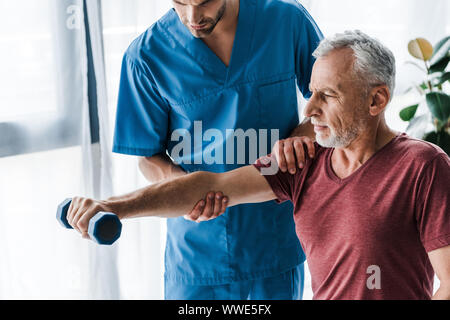 7/8-Ansicht der Arzt in der Nähe von reifen Mann mit Hantel in Klinik Stockfoto