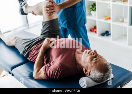 7/8-Ansicht von Arzt berühren Bein reifer Mann Ausbildung auf dem Massagetisch Stockfoto