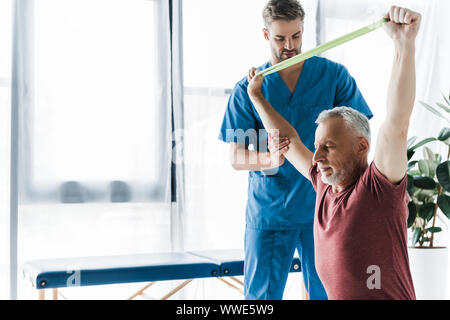 Arzt in der Nähe von mittleren gealterten Mann Trainieren mit Widerstand Band Stockfoto