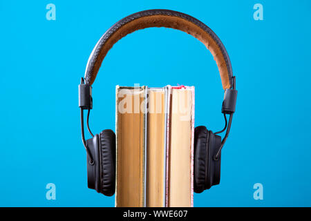 Kopfhörer und Bücher, sondern gegen den blauen Hintergrund, Konzept der Audiobücher, Zuhören, ein Buch Stockfoto