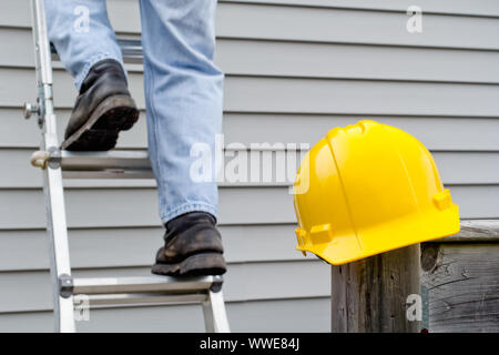 Gelbe hardhat am Geländer Pfosten mit den Beinen des Arbeitnehmers auf Leiter im Hintergrund. Stockfoto