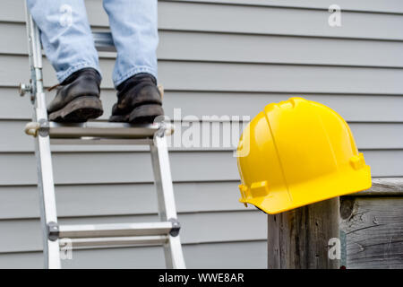 Gelbe hardhat am Geländer Pfosten mit den Beinen des Arbeitnehmers auf Leiter im Hintergrund. Stockfoto