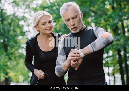 Reife Sportler auf Fitness Tracker in der Nähe von lächelnden Sportlerin überrascht Stockfoto