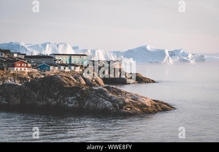 Luftaufnahme der arktischen Stadt Ilulissat, Grönland bei Sonnenaufgang Sonnenuntergang mit Nebel. Bunte Häuser im Zentrum der Stadt mit Eisbergen in der Stockfoto