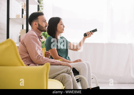 Hübscher junger Mann Fernsehen mit Behinderten Freundin, während auf dem Sofa zu Hause sitzen Stockfoto