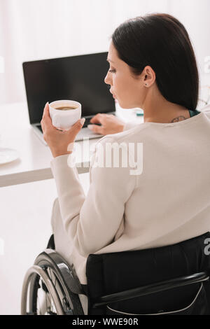 Rückansicht des deaktiviert Geschäftsfrau holding Tasse Kaffee während mit Laptop im Büro Stockfoto