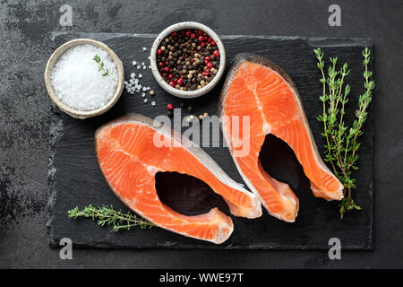 Lachssteaks, Gewürze und Kräuter zum Kochen auf einem schwarzen Schiefer Hintergrund, Ansicht von oben Stockfoto